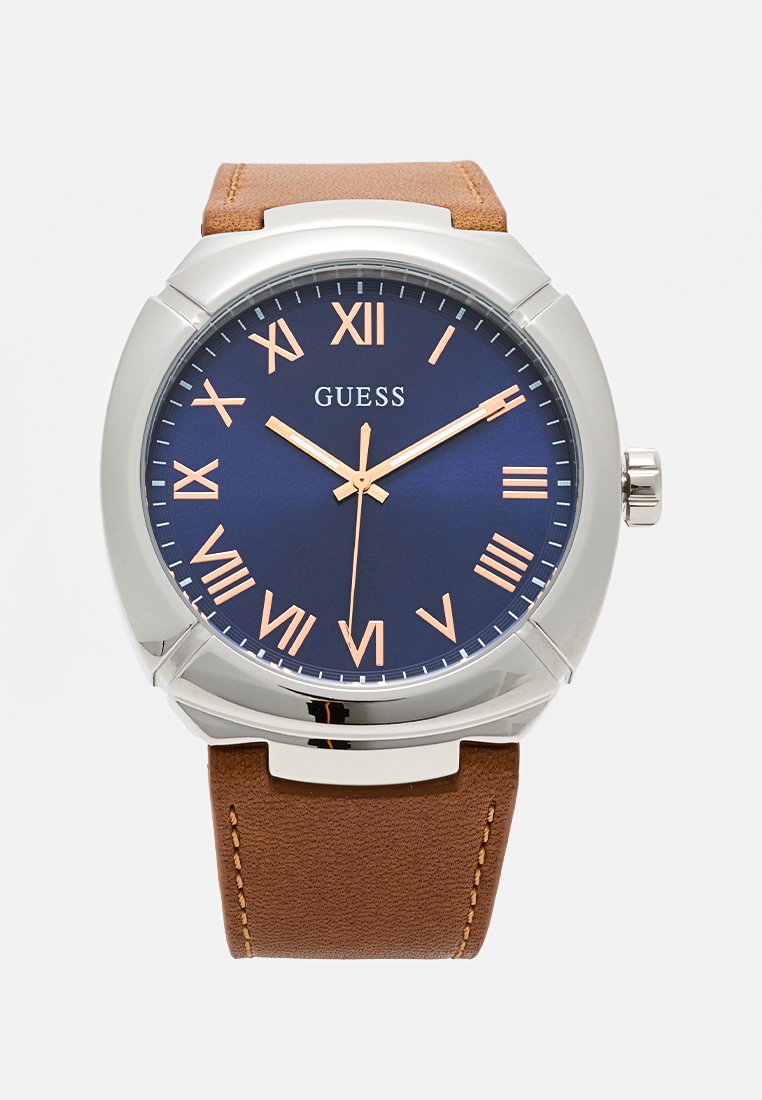 Reloj con correa de cuero marrón, caja de plata, esfera azul, números romanos y manecillas en oro rosa. Cuenta con una corona para ajustar la hora.