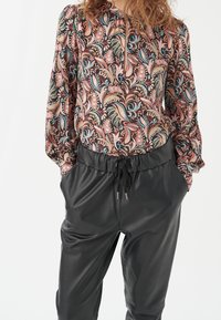 Chemisier à manches longues avec un motif floral rose, bleu et crème, associé à un pantalon en cuir noir avec une taille élastique et un cordon de serrage.