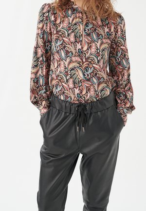 Chemisier à manches longues avec un motif floral rose, bleu et crème, associé à un pantalon en cuir noir avec une taille élastique et un cordon de serrage.