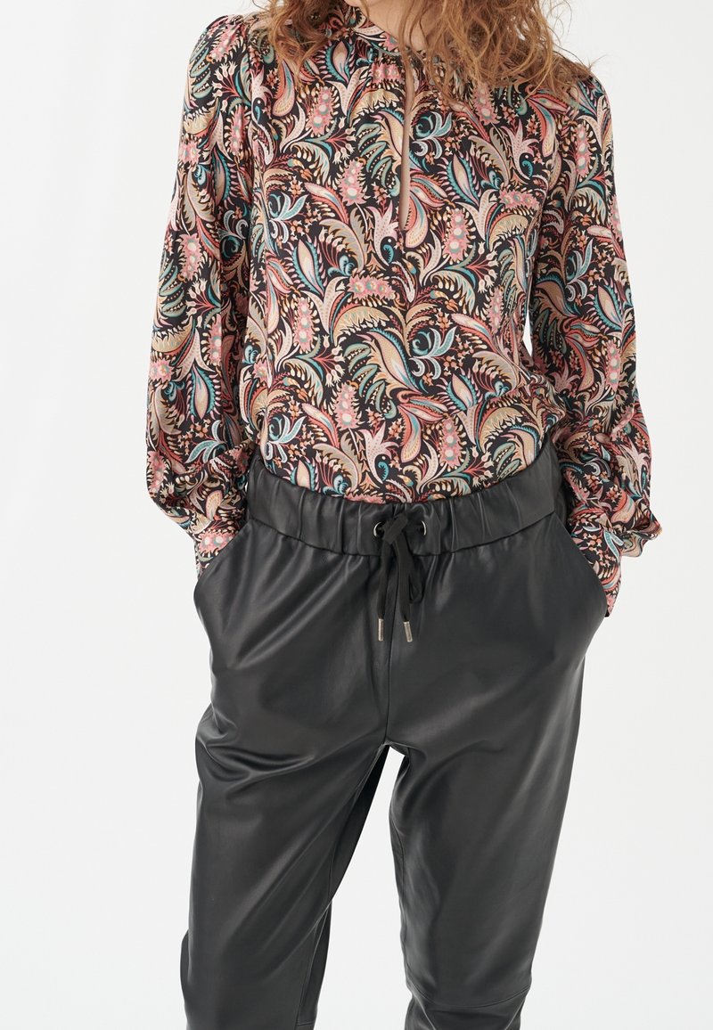 Chemisier à manches longues avec un motif floral rose, bleu et crème, associé à un pantalon en cuir noir avec une taille élastique et un cordon de serrage.