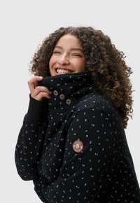 Design di felpa nera con motivi geometrici in rosa, grigio e bianco. Collo alto con chiusura a tre bottoni, patch rotondo con logo sulla manica.