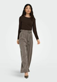 Bruine lange mouwtop gecombineerd met hoge taille, geplooide grijze broek met een strikceintuur, een gladde textuur en taps toelopende benen.