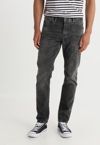 Vaqueros de mezclilla negra con un acabado desgastado y rasgado, de corte ajustado, diseño de cinco bolsillos y cierre de botón, combinados con zapatillas de lona negras.