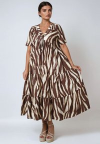 Brown and cream tiered maxi dress with a v-neckline, short sleeves, and a drawstring detail, featuring a bold zebra stripe pattern.