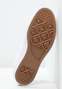 Zapatillas de lona blancas con suela de goma que presentan un patrón hexagonal marrón y la marca "Converse All Star". Acentos de goma visibles en el costado y el talón.