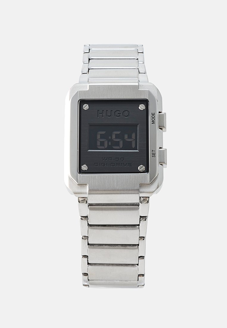 Reloj digital de pulsera de metal plateado con esfera rectangular negra que muestra la hora 6:54, etiquetado como "HUGO", con botones laterales para el modo y la configuración.