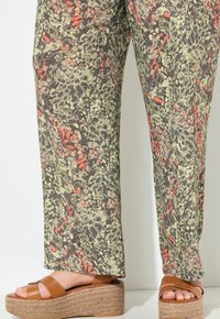 Pantaloni a gamba larga con una audace stampa leopardata in tonalità di verde, marrone e arancione. Abbinati a sandali con piattaforma color cuoio e suola texturizzata.