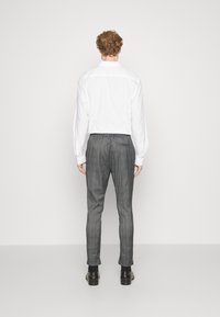 Vit långärmad skjorta, grå rutiga byxor med elastisk midja, slim fit och avsmalnande ben, kombinerat med svarta dressade skor.