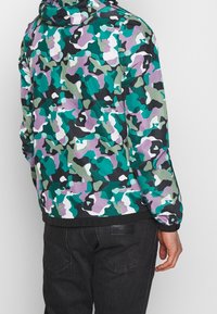 Hoodie jas in een camouflagepatroon met tinten groen, paars en zwart. Elastische manchetten en boord; lichtgewicht stof.