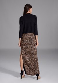 Schwarzes Top mit drei Viertelärmeln, kombiniert mit einem Maxirock im Leopardenmuster mit seitlichen Schlitzen, getragen mit schwarzen High Heels.