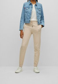Jeansjacke mit Fronttaschen, hellblaue Farbe, kombiniert mit beigen elastischen Sweatpants mit Kordelzug und weißen Sneakers.