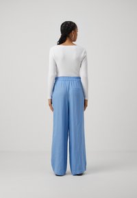 Haut à manches longues blanc rayé et pantalon large bleu clair avec taille élastique. Le pantalon dispose d'une poche arrière. Texture de tissu lisse.
