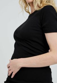 Black ribbed short-sleeve T-shirt fitted to the body; smooth texture; worn by a person with a light complexion, hand resting on abdomen.