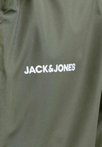Maslinasto zelena tkanina s bijelim natpisom "JACK&JONES" koji označava marku, prikazujući dio odjevnog predmeta.