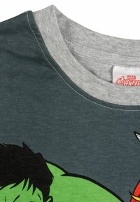 T-shirt grigio scuro con colletto grigio, con un design verde e nero sul fronte. Materiale in cotone morbido con dettagli di cucitura visibili.