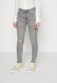 Vaqueros ajustados grises con una rodilla desgastada, diseño de cintura alta y cinco bolsillos, combinados con zapatillas de plataforma crema.