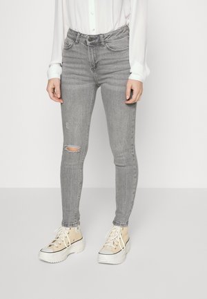 Vaqueros ajustados grises con una rodilla desgastada, diseño de cintura alta y cinco bolsillos, combinados con zapatillas de plataforma crema.