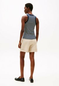Top sin mangas a rayas en azul marino y blanco con un diseño ajustado, combinado con pantalones cortos beige claros y mocasines negros. Textura suave, estilo casual.