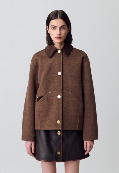 Chaqueta de mezcla de lana marrón con cuello de pana, grandes bolsillos frontales y botones dorados, combinada con una falda de cuero negra que presenta detalles de botones.