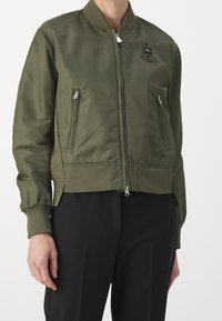 Olivově zelená bomber bunda s předním zipem, dvěma zipovými kapsami, žebrovanými manžetami a pasem. Hladký, mírně lesklý materiál.