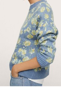 Blauer Pullover mit Blumenmuster in Gelb und Grün. Gerippter Halsausschnitt und Bündchen, strukturierter Strick. Kombiniert mit hellen Jeans.