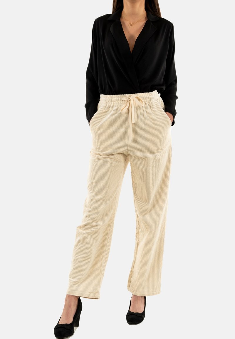 Beige corduroy broek met een trekkoord in de taille en twee zijzakken, gecombineerd met een zwarte blouse met lange mouwen en zwarte hakken.