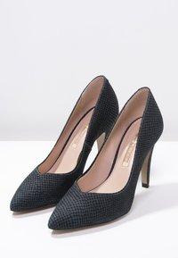 Escarpins noirs avec une finition texturée, un design à bout pointu et un talon aiguille de 10 cm, présentant une doublure intérieure rose.