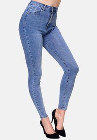 Jeans ajustados de cintura alta en denim azul claro con una textura suave. Cuenta con cinco bolsillos y cierre de cremallera, combinados con tacones negros.