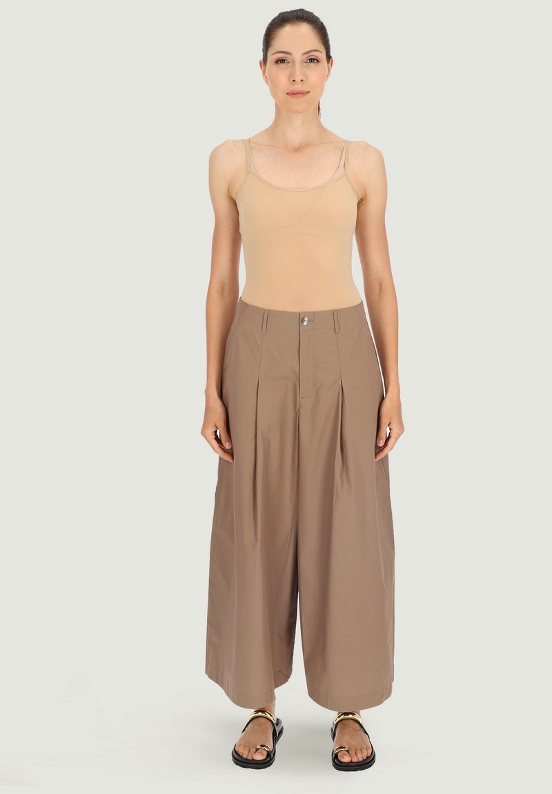 Beżowy top na ramiączkach i brązowe szerokie spodnie z zakładkami i guzikiem z przodu. Czarne sandały z ozdobnym paskiem.