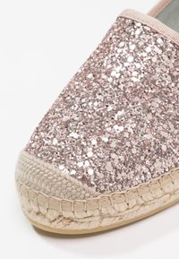 Gros plan sur une espadrille rose pailletée avec une semelle en jute tissé et des détails de couture beige.