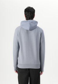 Sudadera con capucha gris claro con un patrón de cuadrícula, que presenta una capucha de contraste en un tono más claro, puños y dobladillo acanalados. Textura suave, ajuste casual.