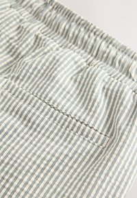 Tela a rayas con líneas azul claro y crema, con una cintura fruncida y una textura fruncida, incluye un detalle de bolsillo trasero.