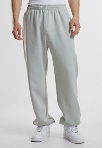 Hellgraue Sweatpants aus weichem Material, mit elastischem Bund und lockerer Passform. Kombiniert mit weißen Sneakers, ohne sichtbare Muster.