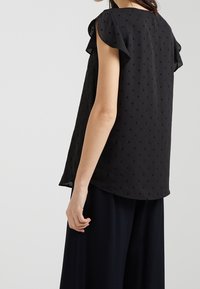 Svart blus med korta volangärmar, med ett strukturerat mönster av små stjärnor, mjukt tyg och en lös passform.