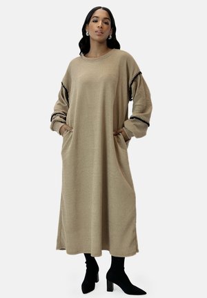 Beige gestreiftes Strickkleid mit langen Ärmeln und Taschen. Schwarzer Besatz an den Ärmelenden. Knielang, kombiniert mit schwarzen Stiefeletten.