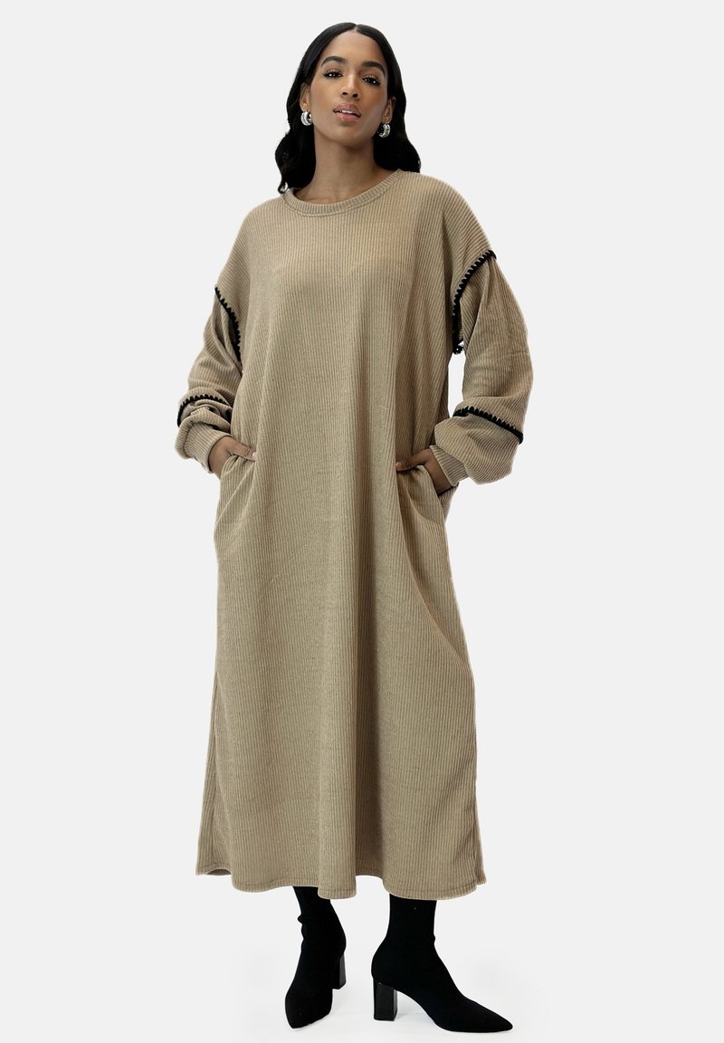 Beige gestreiftes Strickkleid mit langen Ärmeln und Taschen. Schwarzer Besatz an den Ärmelenden. Knielang, kombiniert mit schwarzen Stiefeletten.