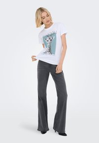 Camiseta blanca de algodón con un gráfico de jirafa y el texto "SAFARI", combinada con pantalones acampanados grises y zapatos de tacón negros. Diseño simple.