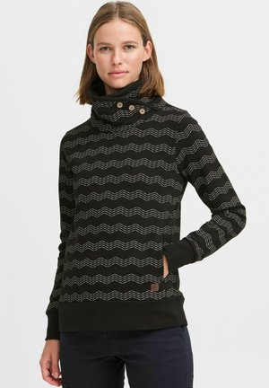 Sweatshirt noir avec un col haut, présentant un motif ondulé blanc, des accents de boutons sur le col et des poches latérales. Tissu doux et design ajusté.