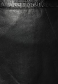 Sort læderstof med en glat tekstur, der har subtile kornmønstre og en ensartet farve over overfladen. Søm detaljer synlige øverst.