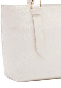 Sac fourre-tout en cuir blanc avec une texture granuleuse, doté d'une bandoulière plate et d'accents en métal doré, de forme rectangulaire et au design structuré.