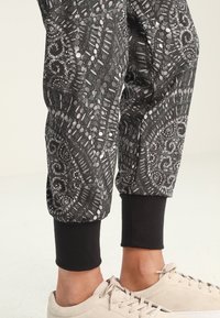 Czarne dresowe spodnie z wzorem, z teksturowanym wykończeniem, zakończone elastycznymi mankietami. W połączeniu z jasnobeżowymi sneakerami dla neutralnego kontrastu.