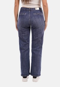 Jeans in denim blu scuro con taglio dritto, dotati di due tasche posteriori, etichetta sulla vita e dettagli di cucitura discreti.