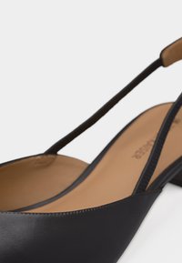 Μαύρο δερμάτινο παπούτσι slingback με μυτερή μύτη, χαμηλό τετράγωνο τακούνι και μαλακό ταμπά ενδιάμεσο πέλμα, απεικονίζεται σε κοντινό πλάνο σε λευκό φόντο.