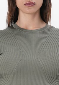 Top a coste verde oliva con scollo a girocollo e cuciture angolari, che mette in evidenza un tessuto morbido e testurizzato. Finitura liscia con dettagli sottili.