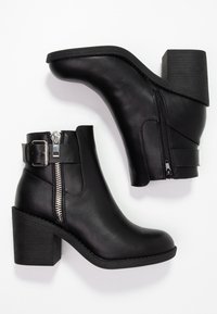 Bottines en cuir noir avec une fermeture éclair, un large talon empilé et une sangle décorative avec boucle. Texture lisse et design élégant.