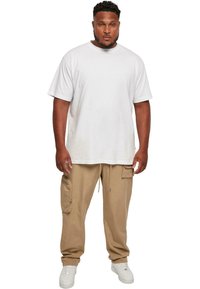 White cotton t-shirt, loose fit, short sleeves. Beige cargo pants with side pocket and adjustable waistband. White sneakers.
