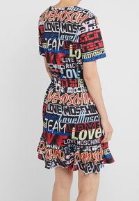 Vestido de manga corta con un estampado gráfico multicolor que incluye texto, con un dobladillo con volante y una silueta ajustada. Está hecho de una tela ligera.