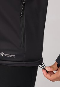 Zwarte Windstopper jas met een rits aan de voorkant, elastische trekkoord in de zoom en een merklabel van Gore-Tex Labs. Gladde textuur, nauwsluitend ontwerp.