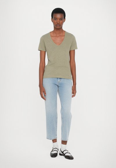 Olivgrön V-ringad T-shirt i mjukt tyg, matchad med ljusblå raka jeans. Svarta lägenheter i blandad textur med vita strumpor.