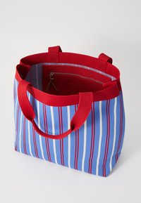 Borsa a tracolla a righe in blu, rosso e bianco. Caratterizzata da robuste maniglie rosse, un interno foderato e una tasca interna con zip per una conservazione sicura.